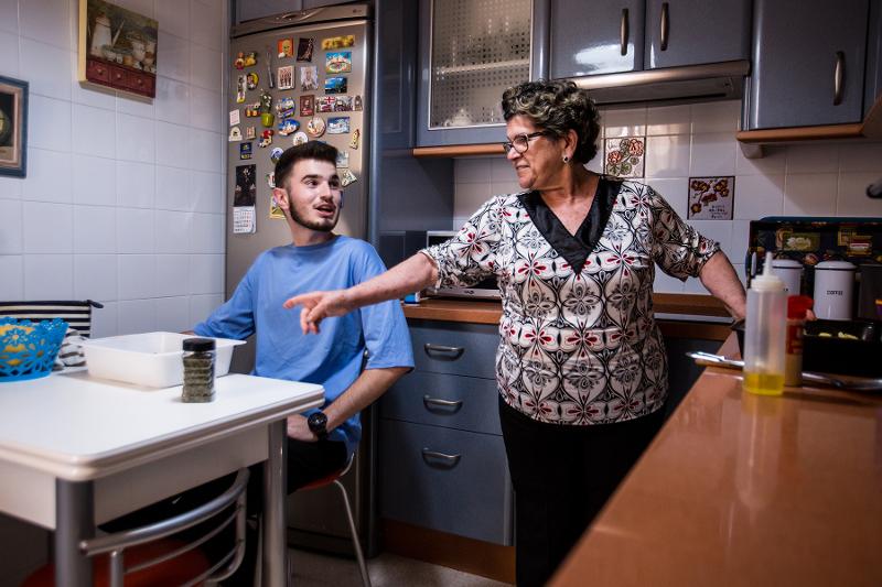 Homem jovem e uma mulher mais velha a conversarem animadamente na cozinha, com utensílios e ingredientes à vista.