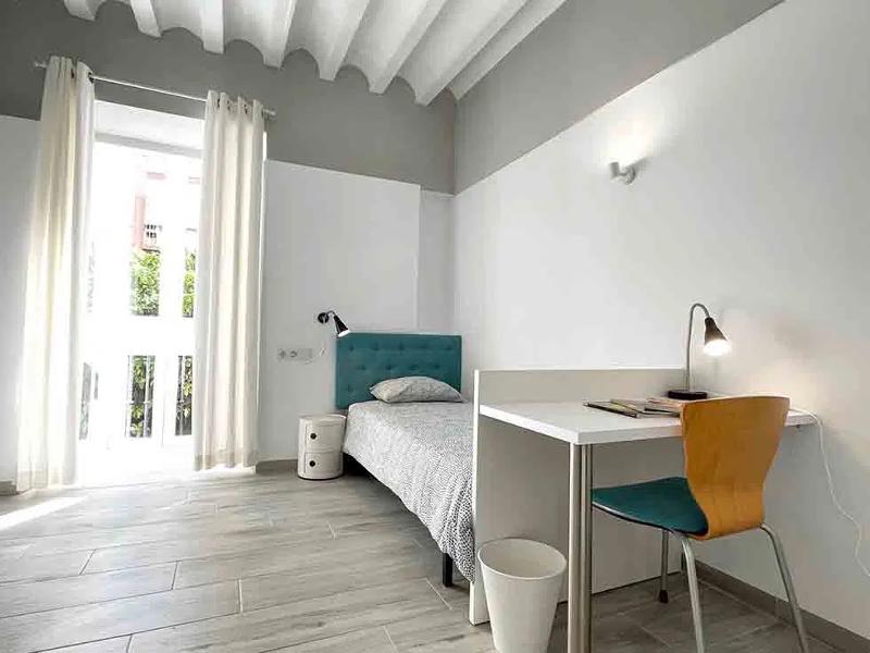 Quarto moderno e luminoso dos cursos de línguas em Espanha, com uma cama simples e uma mesa de estudo.