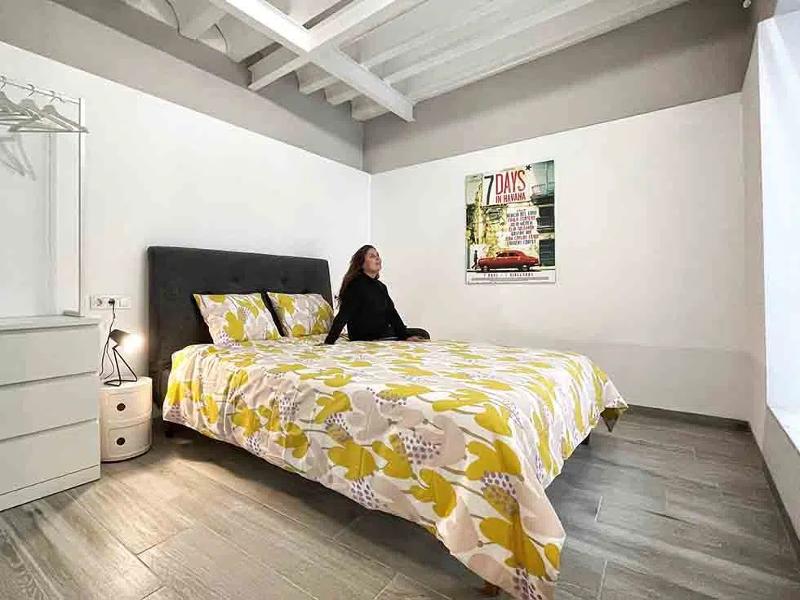 Aluna sentada na cama de um quarto moderno e acolhedor dos cursos de línguas em Espanha, com decoração colorida.