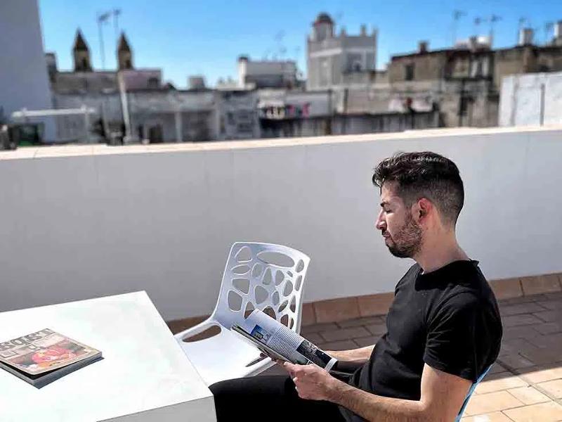 Estudante a relaxar ao sol enquanto lê uma revista nos cursos de línguas em Espanha, com uma vista agradável da cidade.