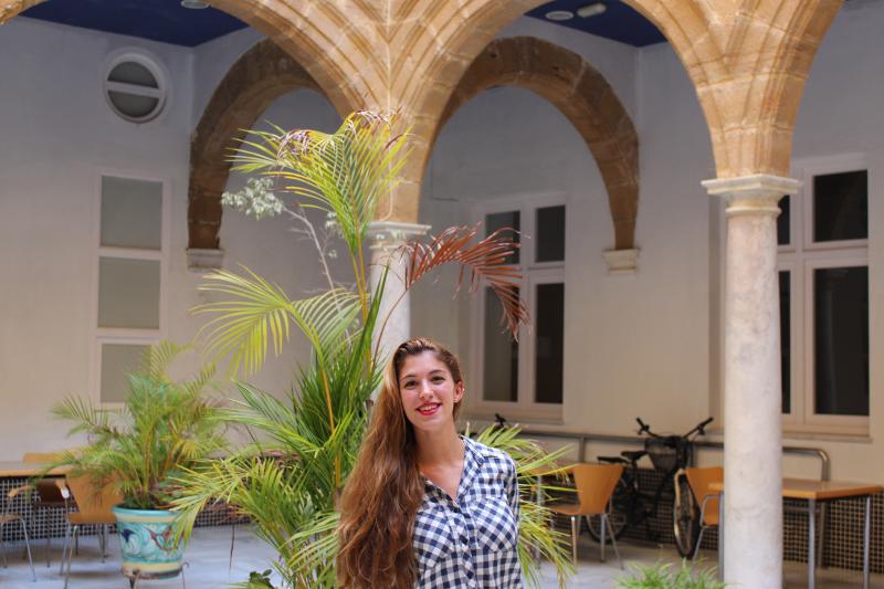  Jovem sorridente em um pátio encantador com colunas clássicas e plantas, ideal para momentos relaxantes durante os cursos de línguas em Espanha.