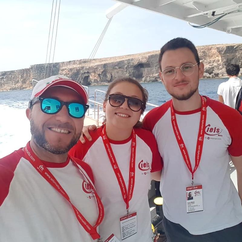 Três monitores a sorrir no barco, a aproveitar o momento com os participantes dos cursos de inglês em malta.