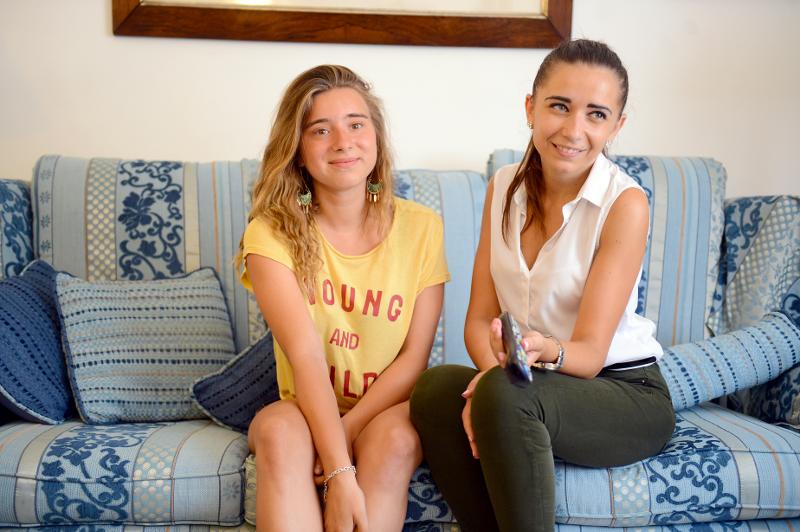 Participante e senhora da família de acolhimento a sorrir, sentadas no sofá da sala, durante os cursos de inglês em malta.
