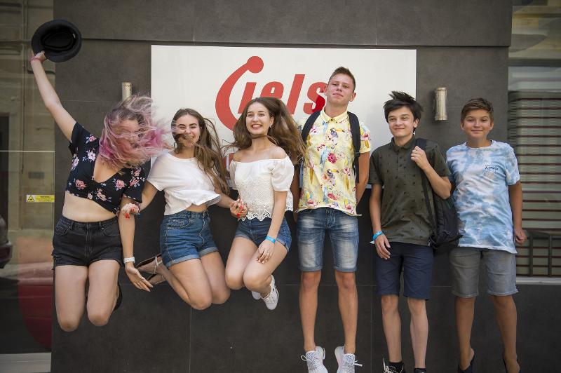 Estudantes a saltar à frente do logo, celebrando o espírito dos cursos de inglês em malta.