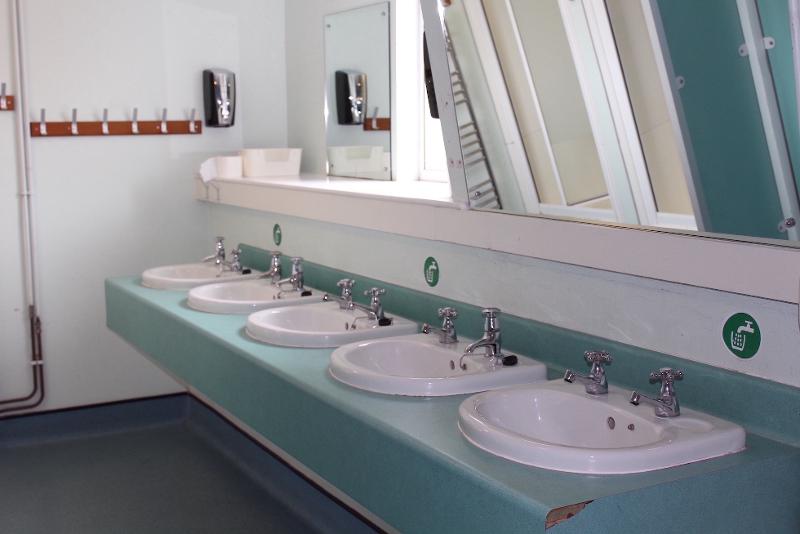 Sala de lavatórios com vários espelhos e torneiras, disponível para participantes de um curso de  ingles para jovens.