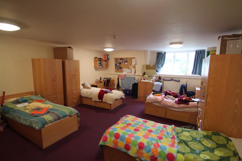 Quarto partilhado com várias camas e decoração pessoal, proporcionando um ambiente acolhedor para jovens num curso de  ingles para jovens.