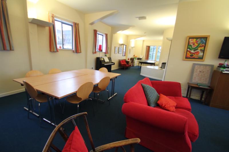 Sala de convívio confortável com mesas, cadeiras e sofás acolhedores, proporcionando um espaço de interação social durante o curso de ingles para jovens.