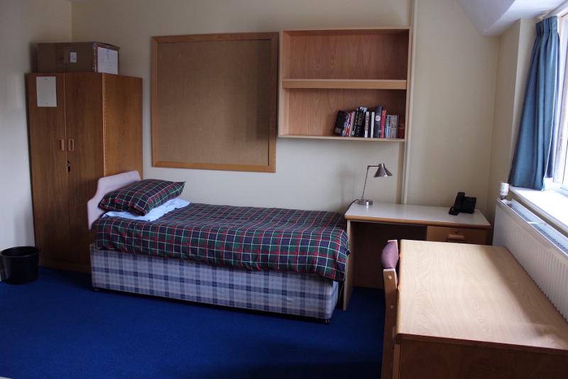 Quarto individual com cama, mesa de estudo e prateleiras, perfeito para relaxar e focar durante o curso de ingles para jovens.