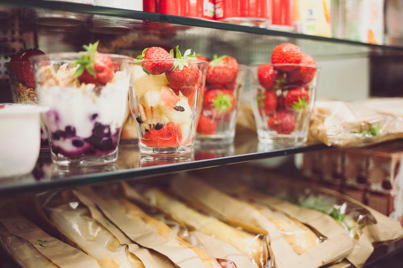 Taças de sobremesa coloridas com frutas frescas e iogurte expostas em uma prateleira, destacando opções saudáveis em um ambiente do curso de ingles para jovens.