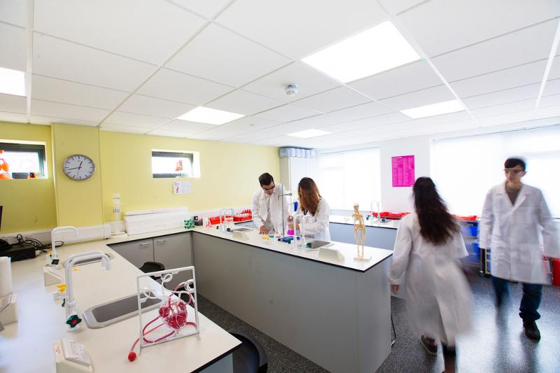 Alunos de lab coat trabalham em experimentos em um laboratório moderno, utilizando equipamentos e frascos coloridos no contexto de um curso de ingles para jovens.