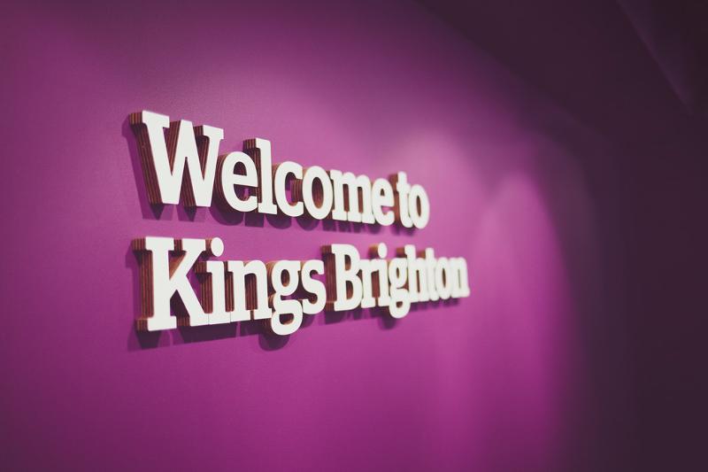 Parede roxa com a mensagem "Welcome to Kings Brighton", acolhendo os visitantes à escola para o curso de ingles para jovens!