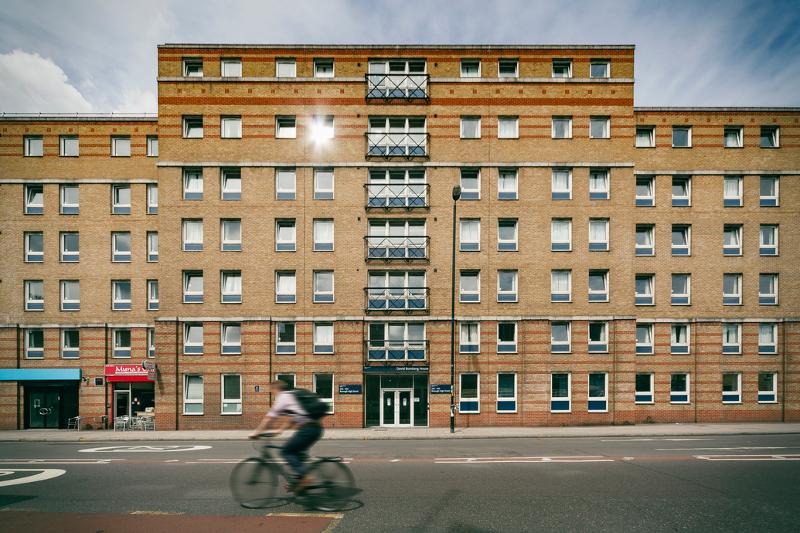 Fachada de um edifício residencial com múltiplas janelas, localizado numa rua movimentada, ideal para estudantes de curso de ingles para jovens.