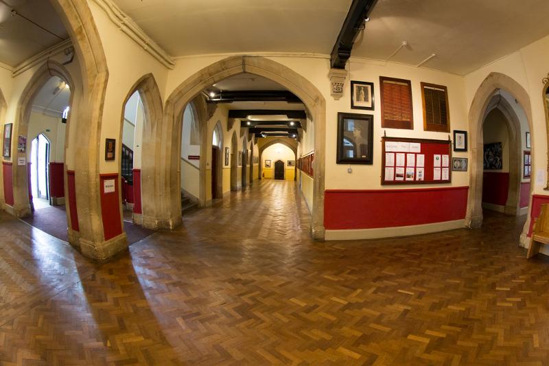 Corredor histórico com piso de madeira e arcos de pedra, usado como espaço de circulação para estudantes de curso de ingles para jovens.