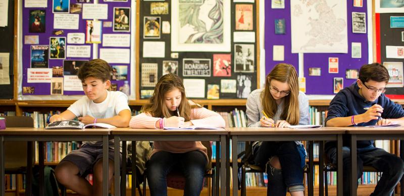Jovens concentrados em atividades de escrita numa sala de aula durante um curso de lingua inglesa.