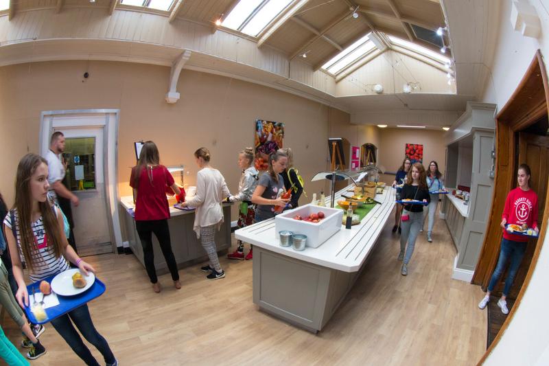 Jovens servindo-se numa cantina iluminada, como parte de um ambiente acolhedor em curso de lingua inglesa.