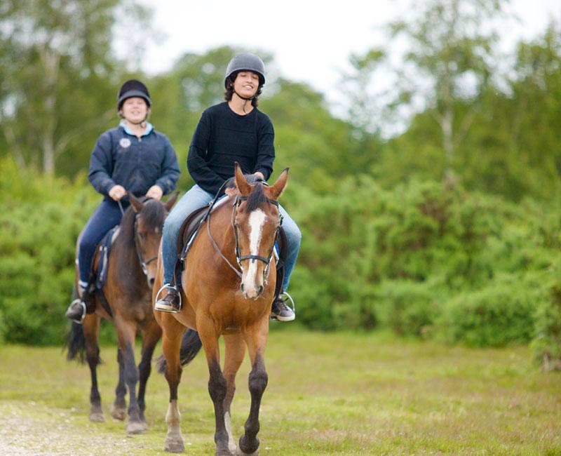 Dois jovens a cavalo, desfrutando de uma experiência ao ar livre durante um curso de lingua inglesa.