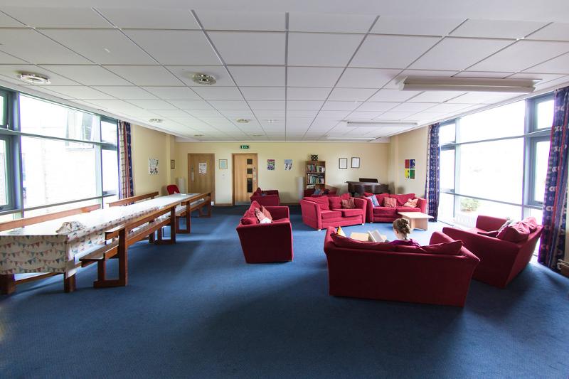 Sala comum espaçosa com sofás vermelhos e áreas de convivência, ideal para estudantes de curso de lingua inglesa.
