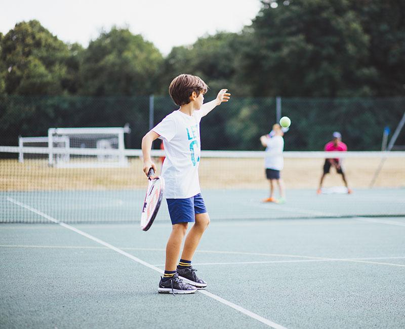 Jovem a praticar ténis num campo ao ar livre, integrando atividades físicas num curso de lingua inglesa.