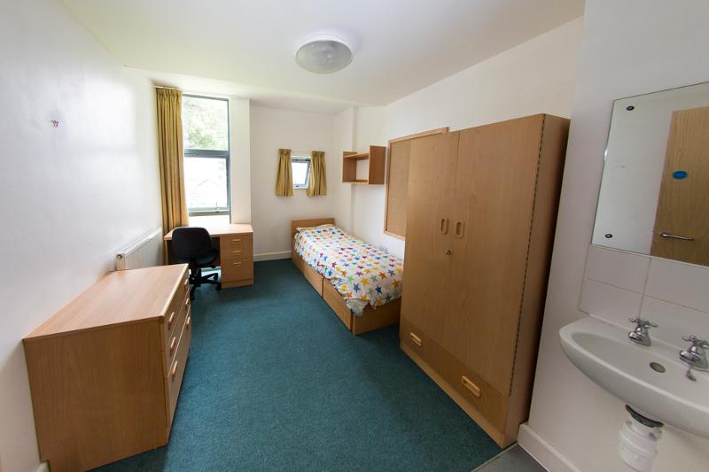 Quarto individual com cama decorada, armário, secretária e janela grande para estudantes de curso de lingua inglesa.