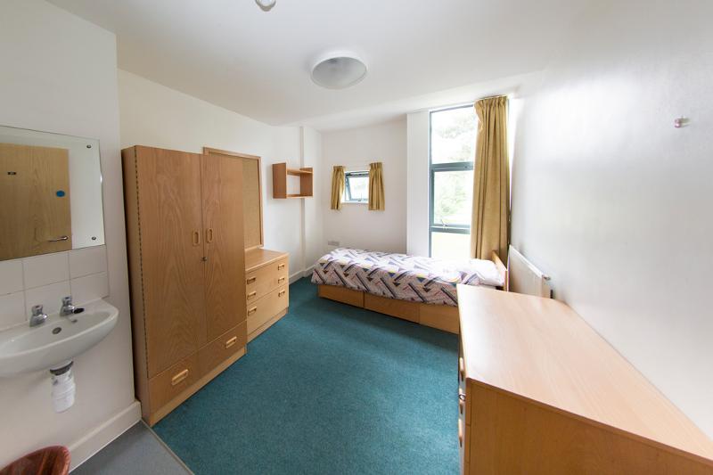 Quarto individual simples e bem iluminado para estudantes de curso de lingua inglesa, com mobiliário básico.
