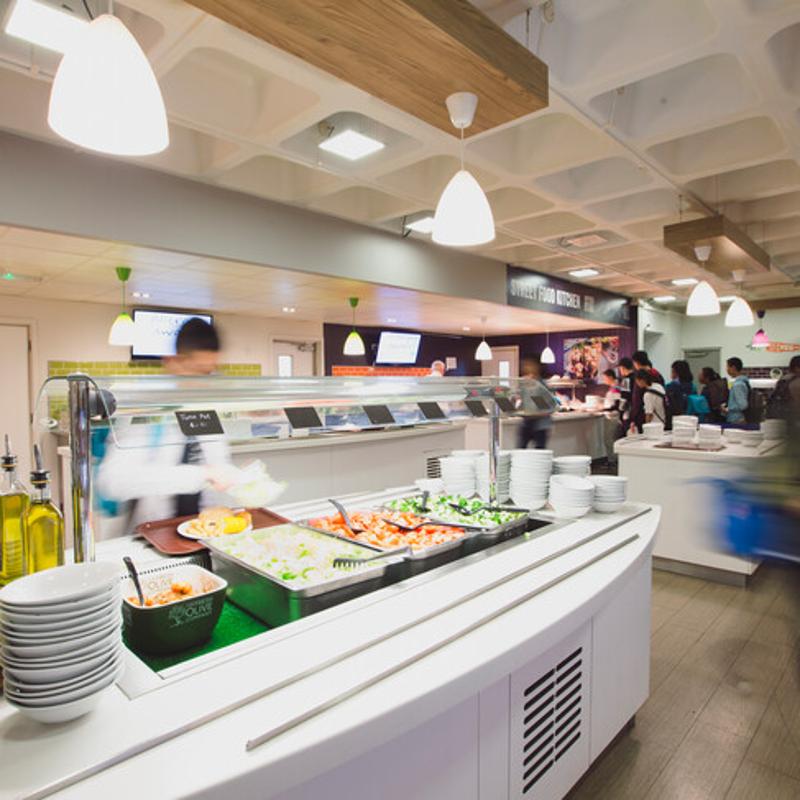 Cantina moderna e movimentada, com uma variedade de pratos frescos e coloridos, ideal para reabastecer energias durante o curso de língua inglesa.