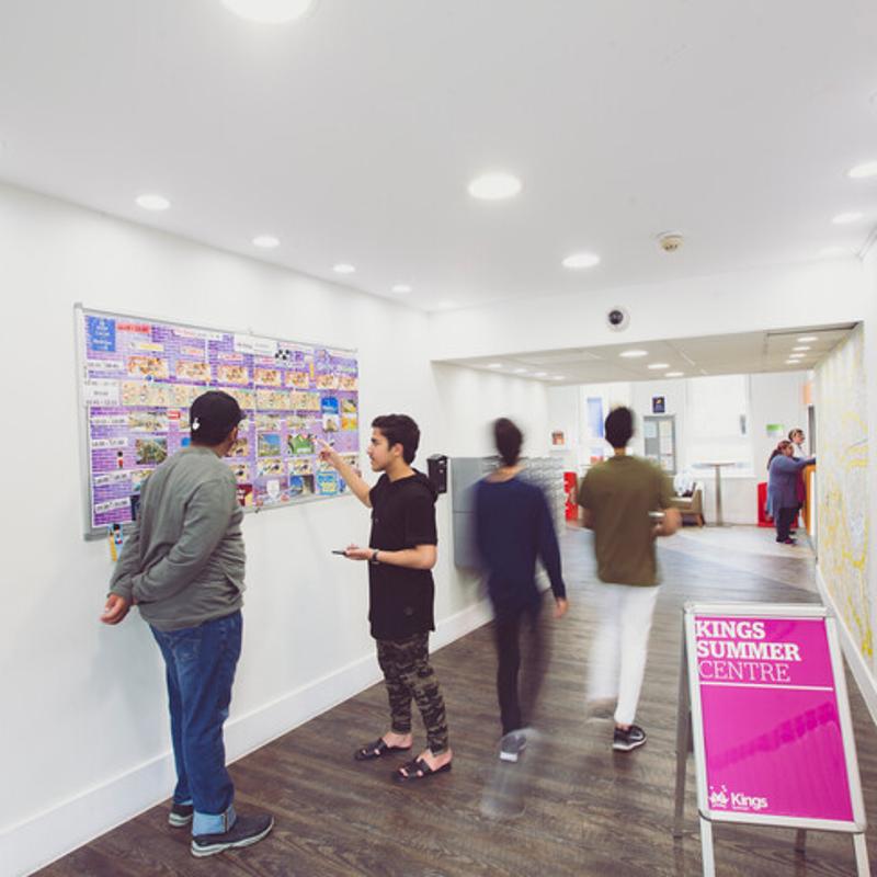 Estudantes observam um quadro de avisos informativo no centro de verão da Kings, planejando as suas atividades durante o curso de língua inglesa.