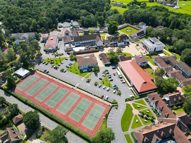 Vista aérea de um complexo que inclui instalações desportivas, com campos de ténis e áreas verdes, perfeito para momentos de lazer durante o teu curso de lingua inglesa.