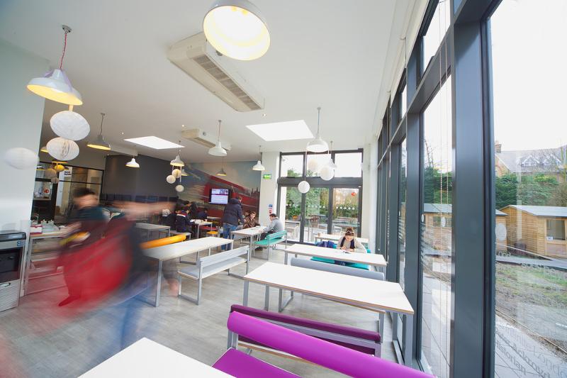 Sala de refeições colorida com bastantes mesas e cadeiras do curso de lingua inglesa