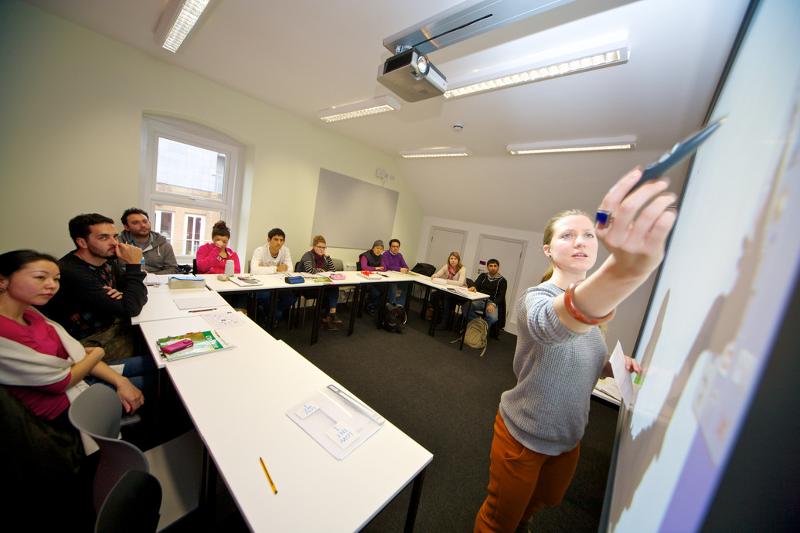 Aula interativa com os alunos a prestarem atenção e a professora a escrever no quadro no curso intensivo de ingles em londres