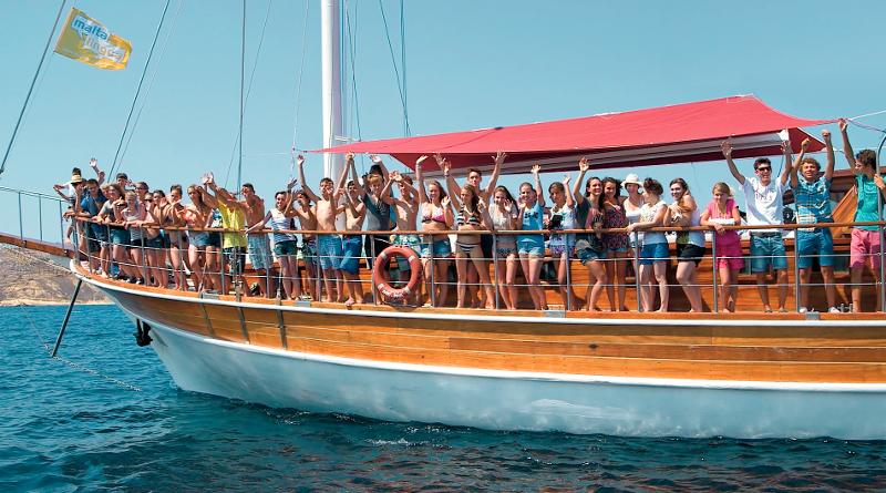 Grupo de estudantes a bordo de um barco, durante um passeio marítimo como parte de um curso de ingles em malta, celebrando com entusiasmo.