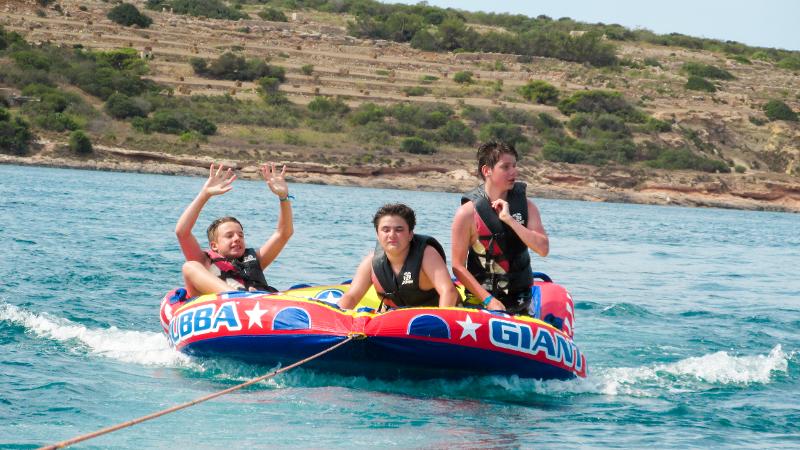Jovens a divertir-se numa boia inflável rebocada durante um curso de ingles em malta, vivenciando momentos de aventura.