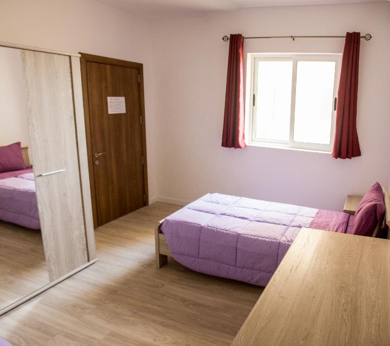 Quarto acolhedor com cama individual e mobiliário moderno para estudantes de um curso de ingles em malta.