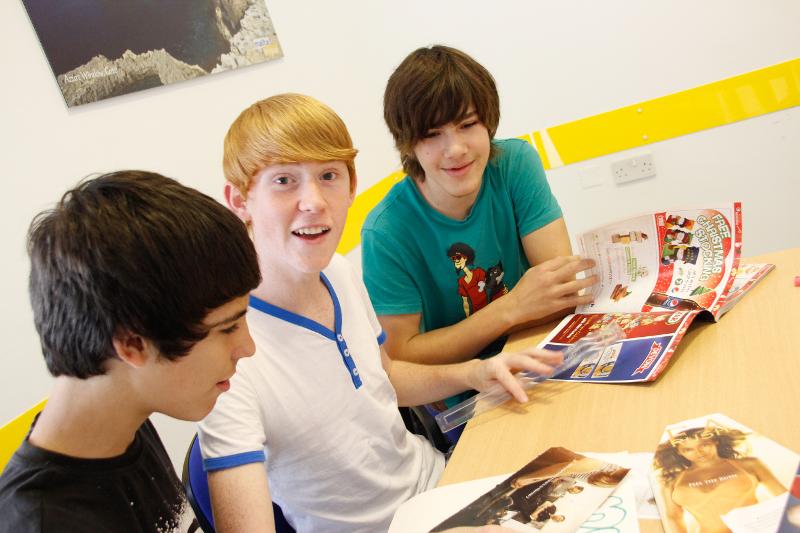 Três jovens a estudar materiais impressos e a interagir durante um curso de ingles em malta, numa aula animada.
