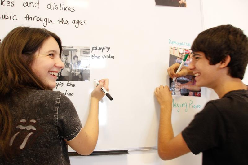 Dois jovens a sorrir enquanto escrevem num quadro branco durante uma atividade de um curso de ingles em malta.