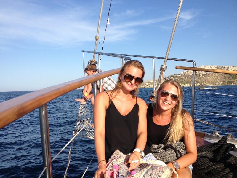 Duas jovens a relaxar a bordo de um barco durante um passeio como parte de um curso de ingles em malta, com vistas de mar ao fundo.