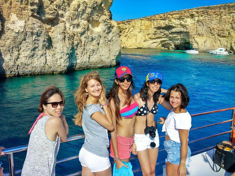Grupo de jovens num passeio de barco, a aproveitar as vistas costeiras como parte de um curso de ingles em malta.