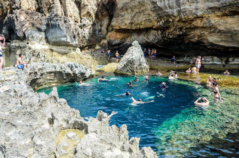 Estudantes a nadar numa piscina natural cercada por rochas durante um curso de linguas em malta, desfrutando da paisagem única