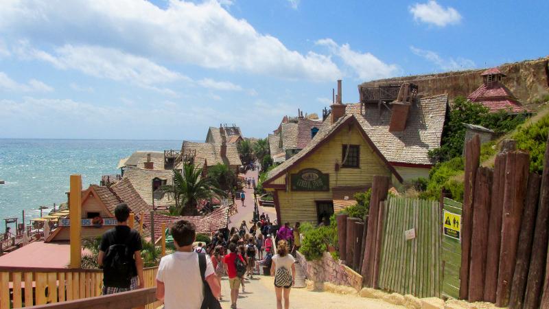 Grupo de estudantes a caminhar por uma vila costeira pitoresca como parte de um passeio cultural de um curso de linguas em malta.