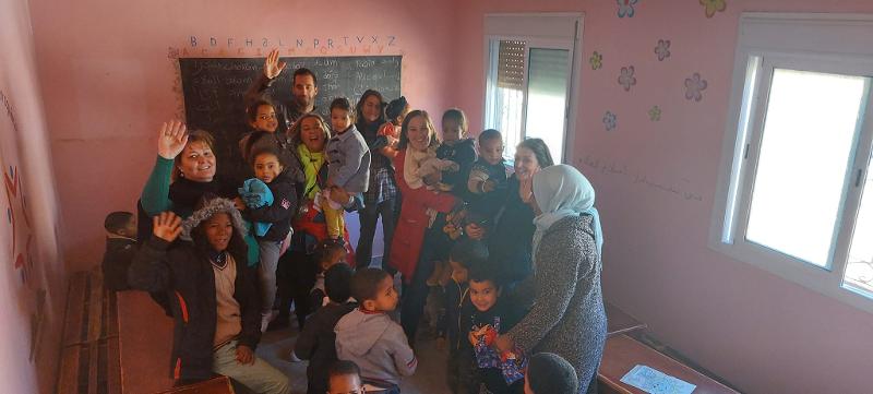 Grupo de crianças e monitores dentro de uma sala de aula felizes a acenar