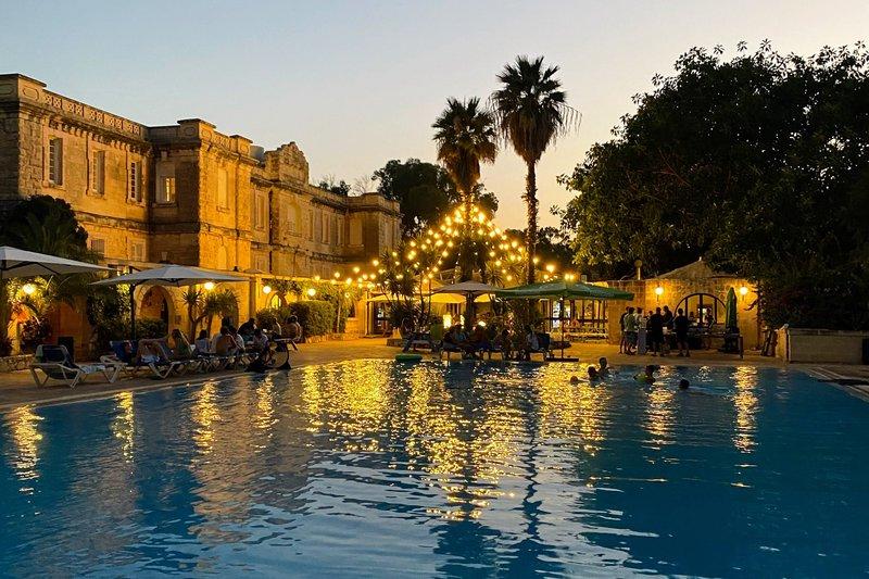Piscina iluminada à noite com pessoas a relaxar e nadar, com luzes decorativas e um ambiente tranquilo do curso de ingles na alemanha.