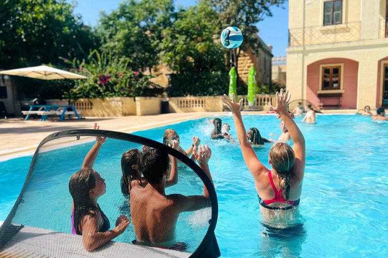 Jovens a jogar um jogo de voleibol na piscina, com um ambiente descontraído e alegre, enquanto participam num curso de linguas na alemanha.
