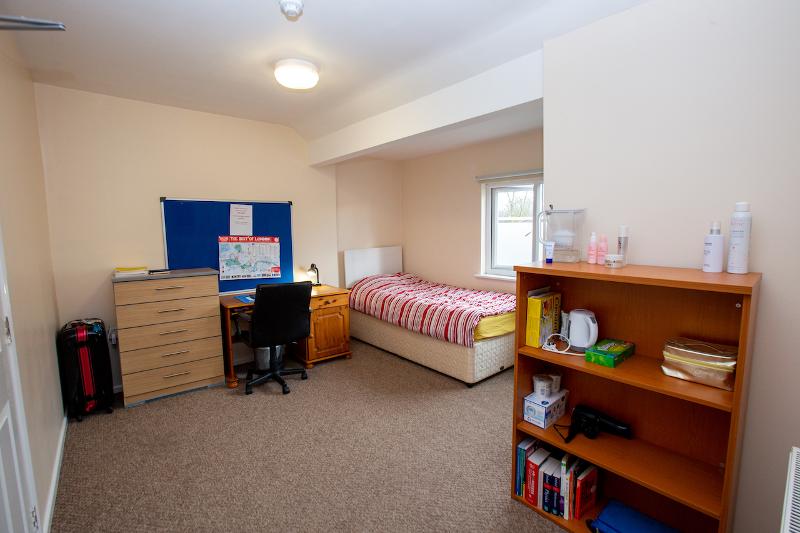 Quarto individual com área de estudo e prateleira, ideal para alunos do curso de ingles cambridge que procuram conforto e foco.