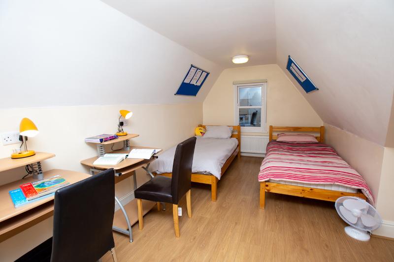 Quarto partilhado com duas camas individuais e áreas de estudo, ideal para alunos do curso de ingles cambridge, promovendo estudo e convivência.