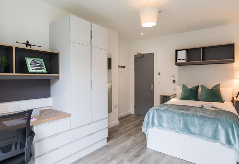 Quarto moderno com cama de casal e área de estudo, parte das acomodações no curso de ingles cambridge, proporcionando conforto e espaço para aprendizagem.