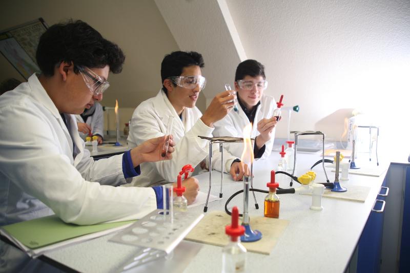 Alunos em laboratório de ciências realizando experiências práticas como parte do curso de ingles cambridge, combinando aprendizagem teórica e prática.