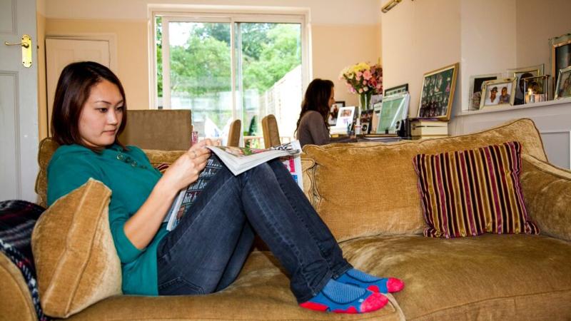 Jovem relaxa no sofá a ler, num ambiente caseiro e acolhedor, como parte do alojamento do curso de língua inglesa.