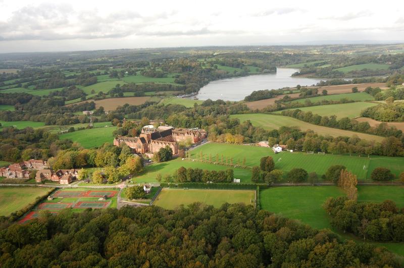 Vista aérea de um vasto campus rodeado por campos verdes e um lago, perfeito para um curso de inglês no estrangeiro.