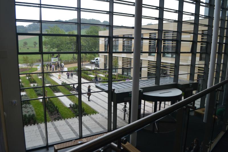 Vista de um edifício moderno com jardim interno através de amplas janelas, proporcionando um ambiente acolhedor para um curso de língua inglesa.