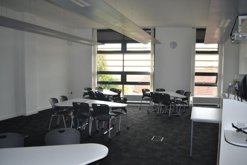 Sala de aula moderna e iluminada com mesas e cadeiras, preparada para atividades de um curso de língua inglesa.