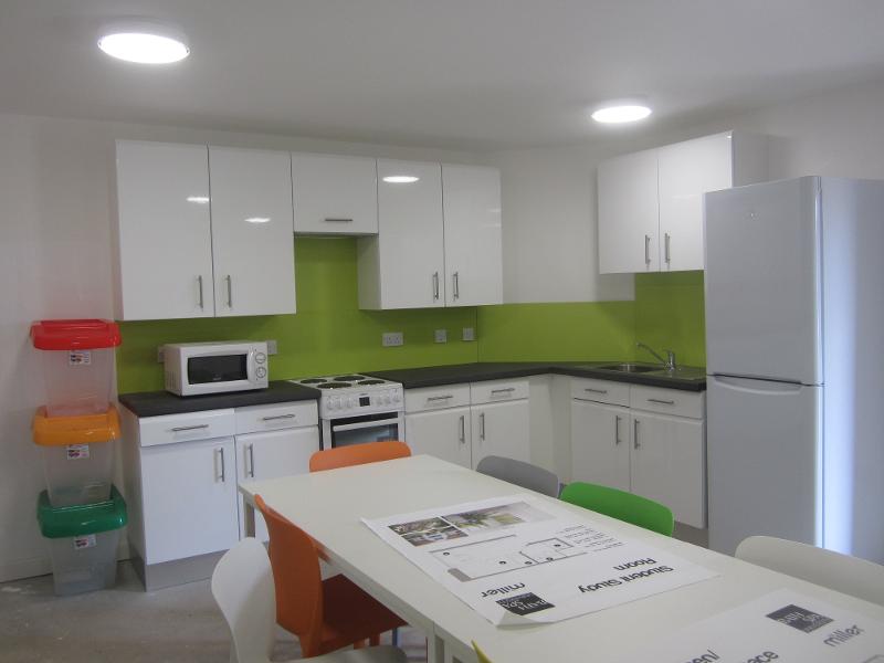 Cozinha comunitária moderna com eletrodomésticos e mesa, ideal para estudantes de um curso de língua inglesa.